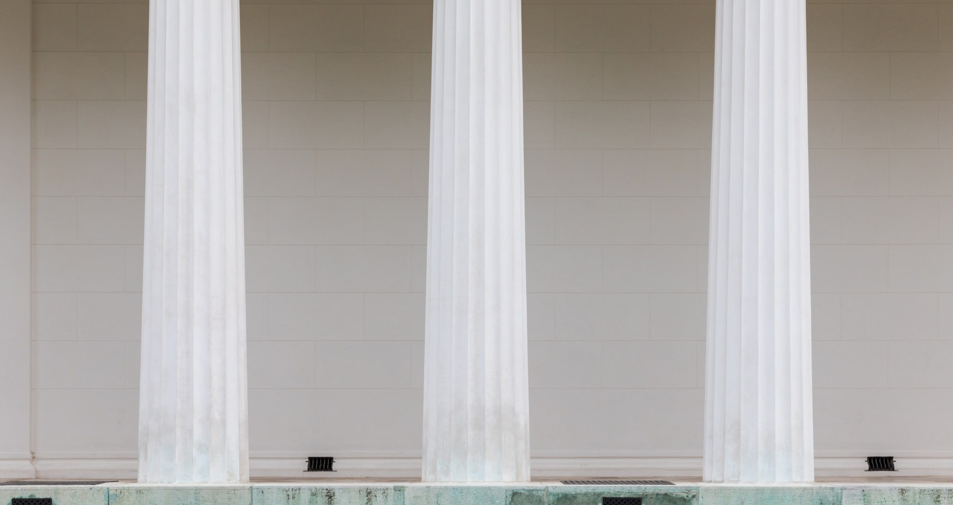 Trois colonnes doriques cannelées blanches devant un mur de pierre clair.